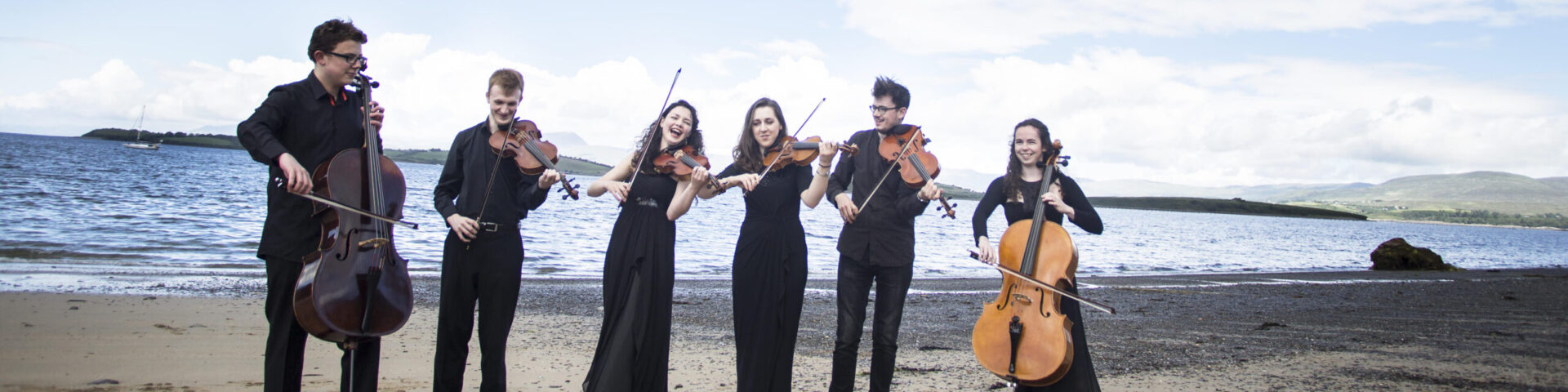 A group of string instrument players on a beach in West Cork