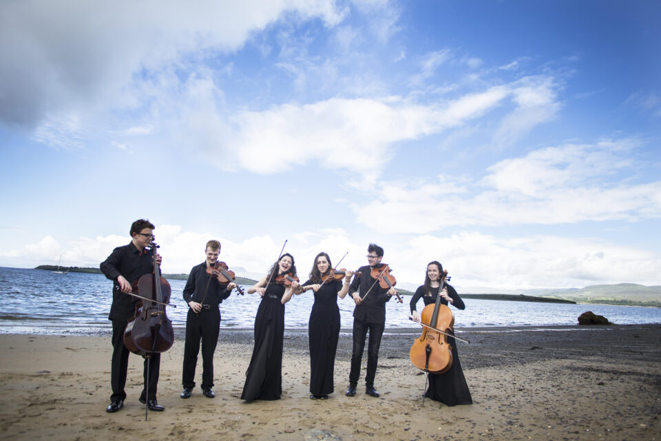 A group of string instrument players on a beach in West Cork